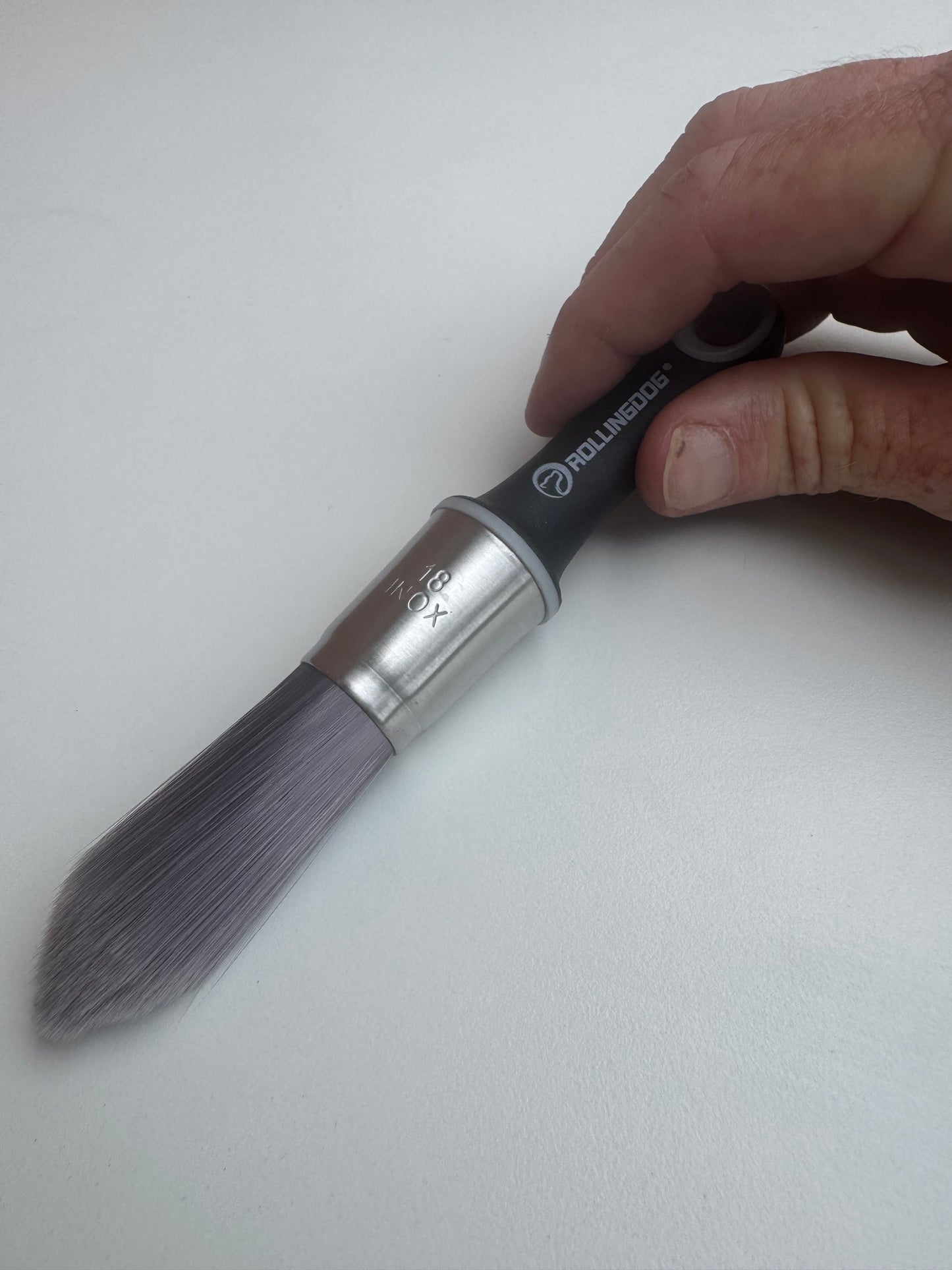 Hand holding a paintbrush with a visible brand logo on a white background